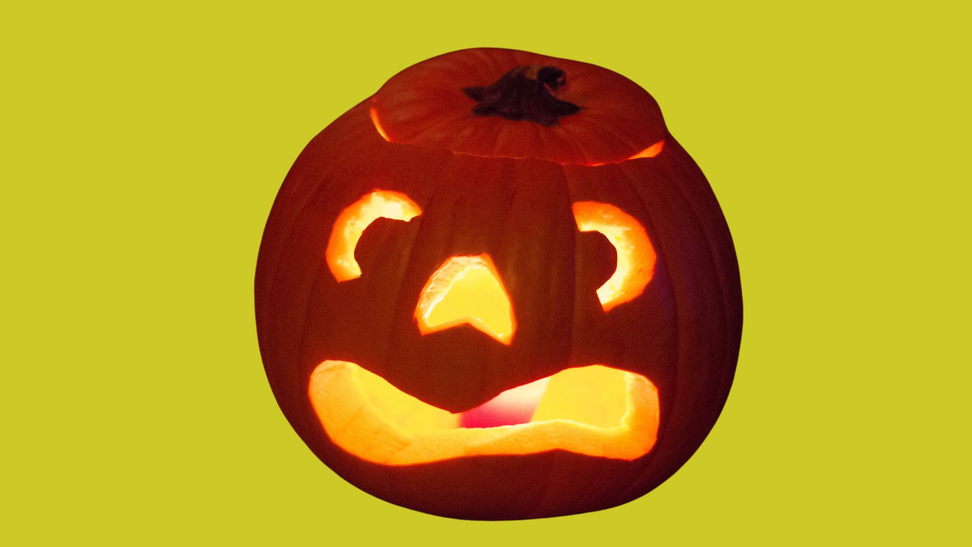 Light pumpkin. Green background. Photo of pumpkin with face carved out lit up