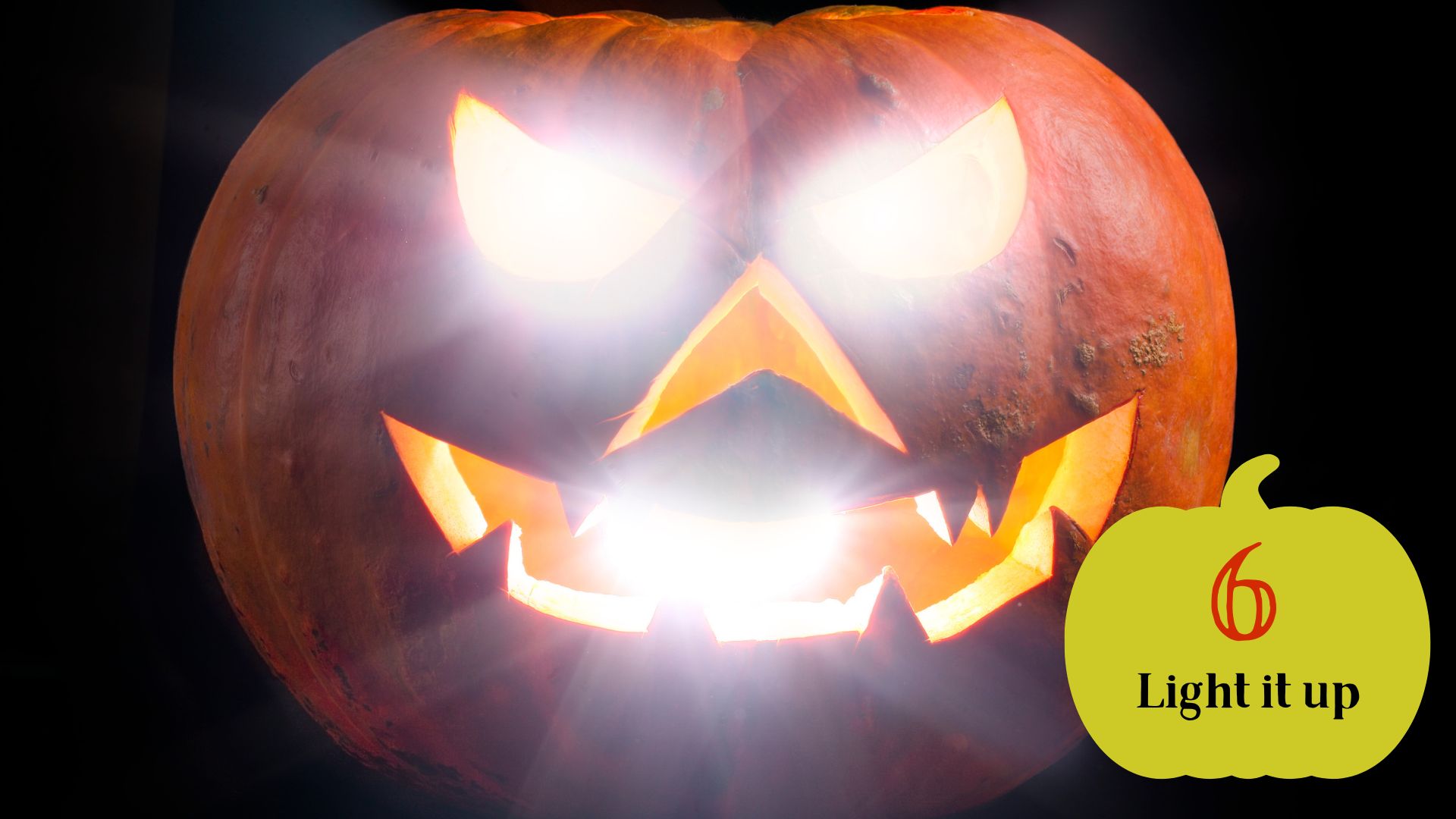 Step 6 of carving a pumpkin is to light it up. Photo of pumpkin with face cut out and light glowing out of face on a black background
